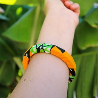 Uma mão a segurar a pulseira bangle azul com padrão africano sobre base rígida de madeira reaproveitada