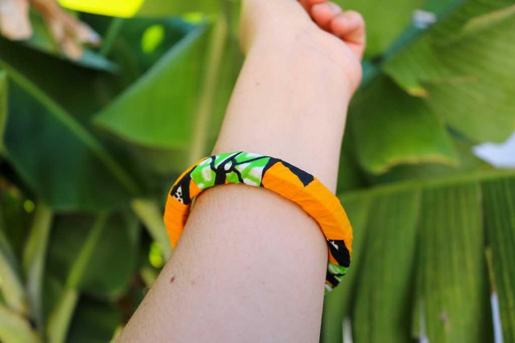 Uma mão a segurar a pulseira bangle azul com padrão africano sobre base rígida de madeira reaproveitada