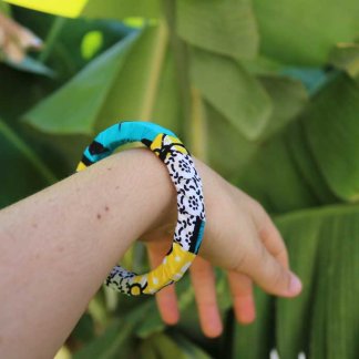 Uma mão a segurar a pulseira colorida com padrão africano sobre base rígida de madeira reaproveitada