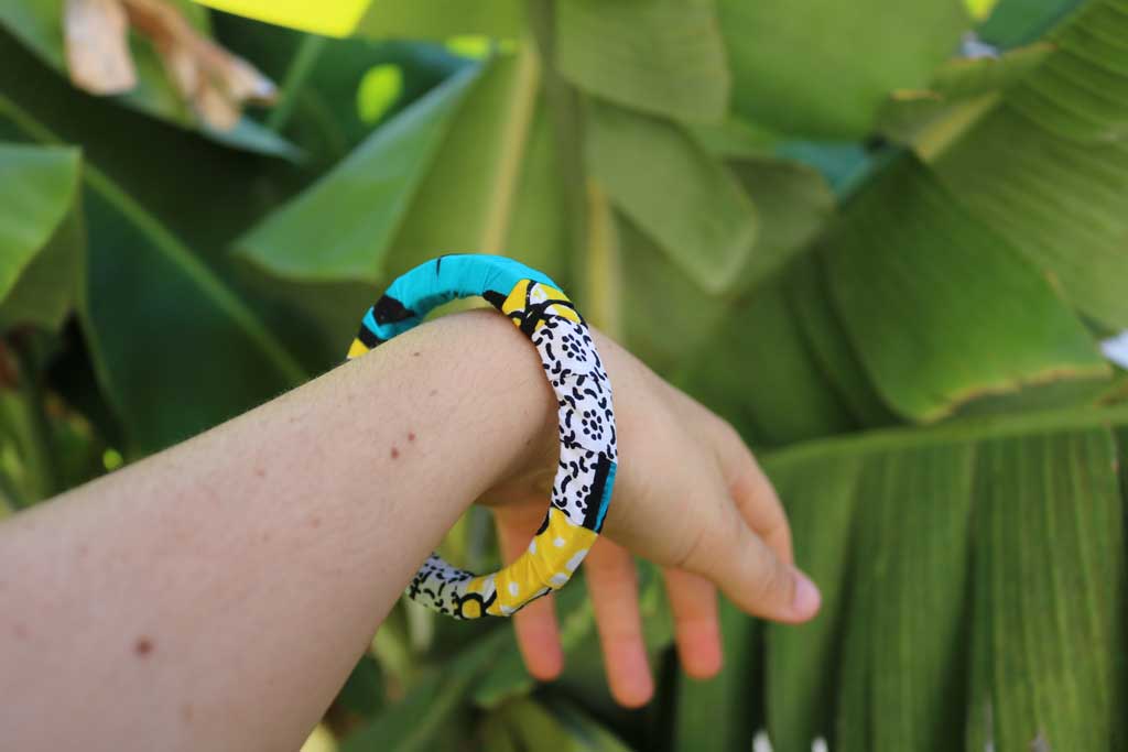 Uma mão a segurar a pulseira colorida com padrão africano sobre base rígida de madeira reaproveitada