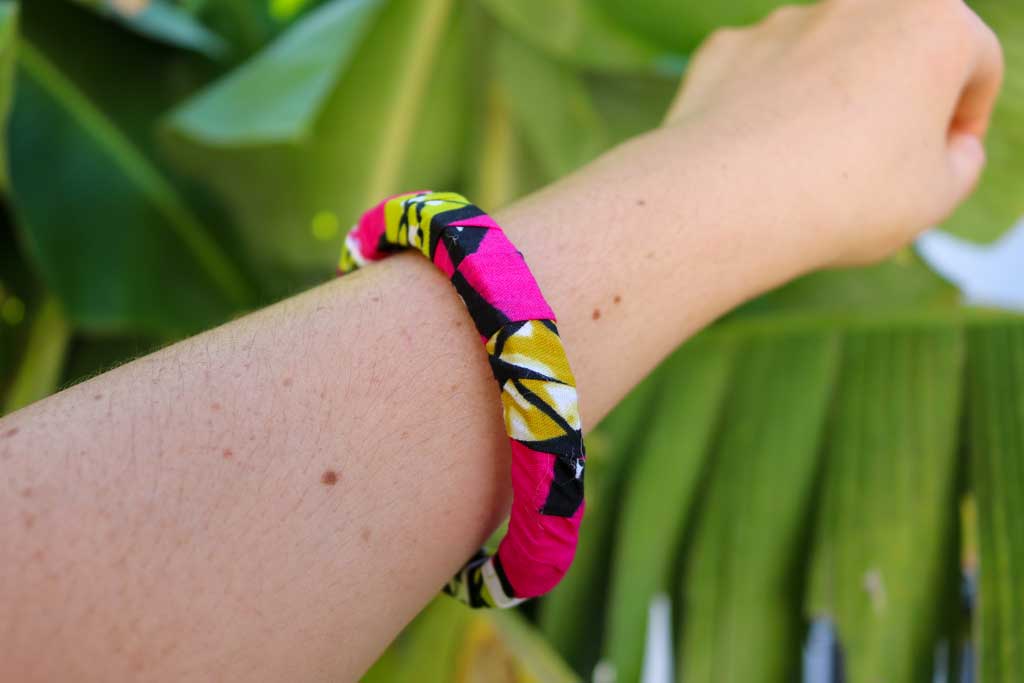 Uma mão a segurar a pulseira étnica com padrão africano sobre base rígida de madeira reaproveitada