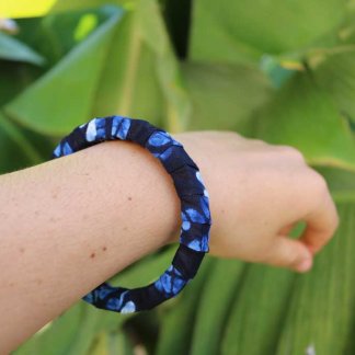 Uma mão a segurar a pulseira artesanal com padrão africano sobre base rígida de madeira reaproveitada