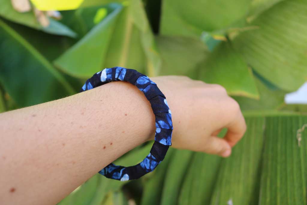 Uma mão a segurar a pulseira artesanal com padrão africano sobre base rígida de madeira reaproveitada