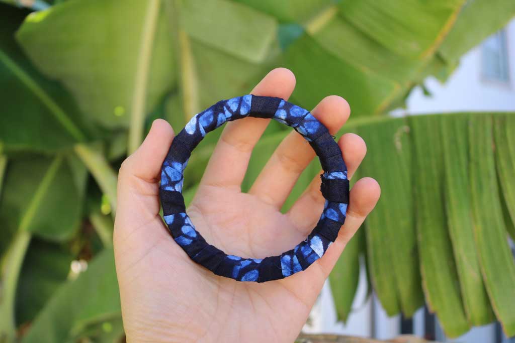 Pulseira artesanal azul com padrão africano sobre base rígida de madeira reaproveitada